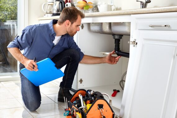 An inspector checking the plumbing under a kitchen sink.