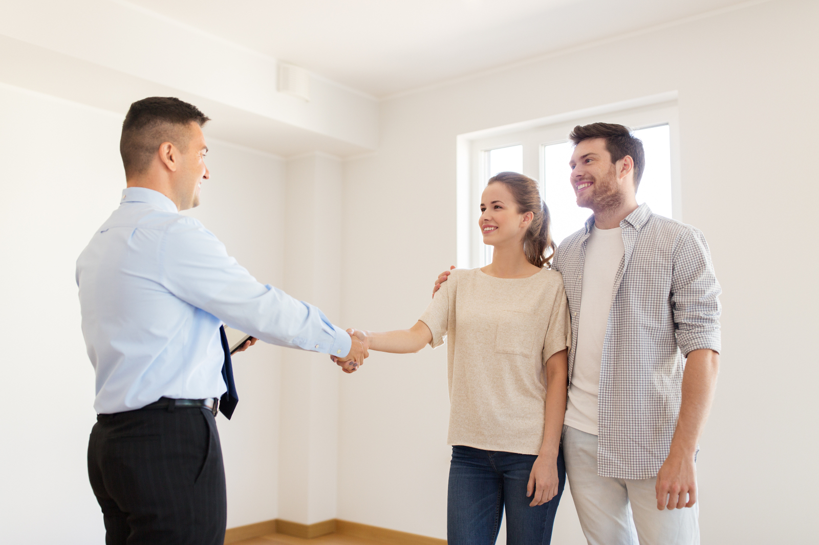 Happy couple and realtor shaking hands at new home to help illustrate home inspection scheduling