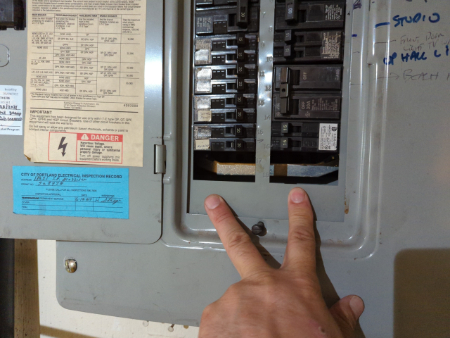 An inspector pointing out open breaker slots in an older electrical panel.